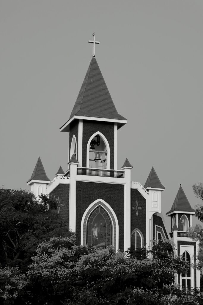 Monochrome image of a church bell tower surrounded by trees, featuring Gothic architecture.